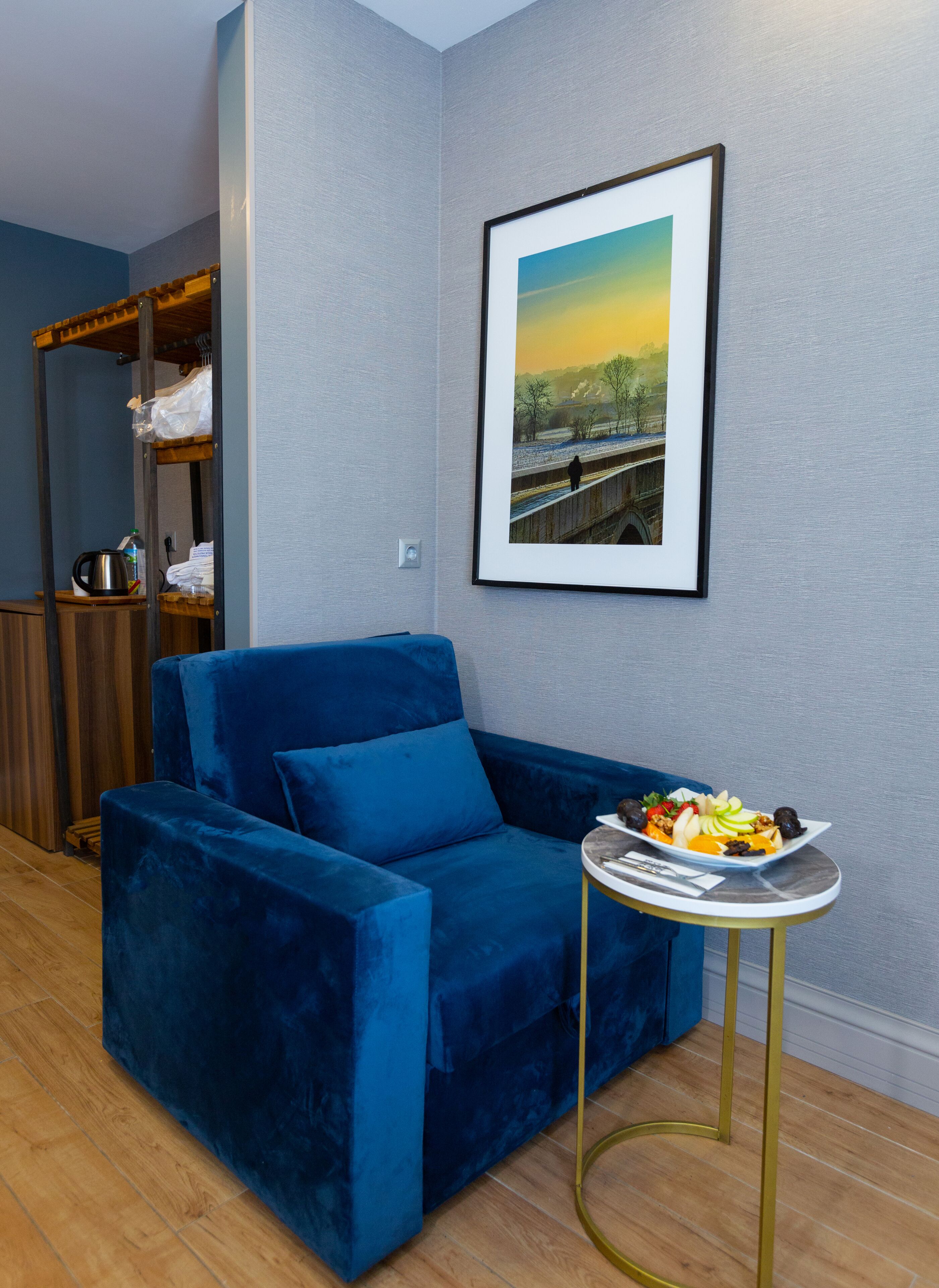A blue velvet sofa, a small round table with a plate of fruit, and a framed picture on the wall.