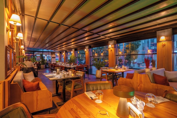 A restaurant with wooden furniture, tables, chairs, and a view of the cityscape through large windows.