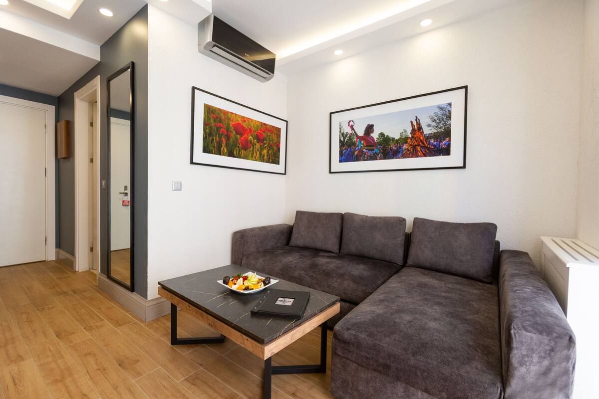 A modern living room with a grey sofa, a wooden coffee table with a plate of fruit, and two framed pictures on the wall.
