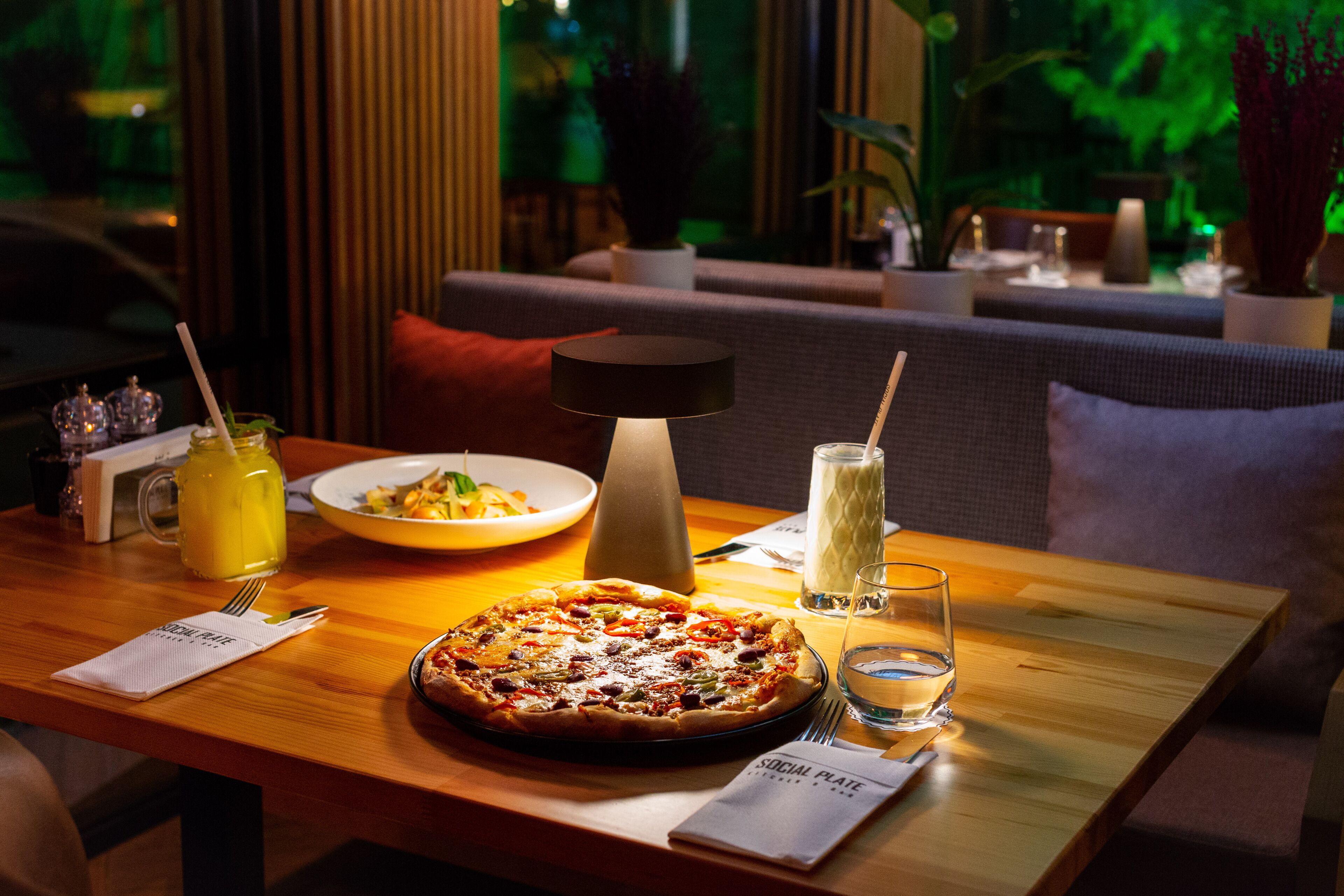 A dining table with a pizza, a pitcher of lemonade, and a candle.