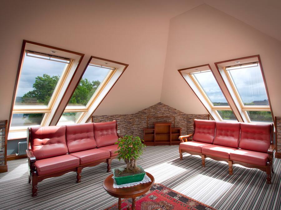 A spacious loft with a high ceiling, large skylights, a stone wall, and a red leather sofa.