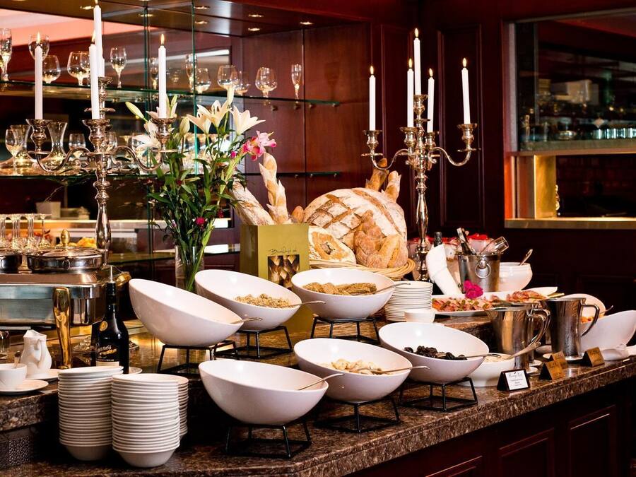 A buffet setup with various food items, including bread, bowls of food, and a variety of glasses.