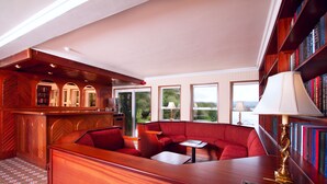 Eine Bibliothek mit Bücherregalen, einem Lesebereich mit Sofa und Tisch sowie einer Bar mit Theke und Sitzgelegenheiten.