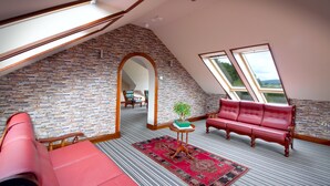 Ein Schlafzimmer im Loft-Stil mit schrägem Dach, freiliegenden Backsteinwänden, einem roten Ledersofa, einem kleinen Tisch mit einer Pflanze und Blick durch große Fenster.