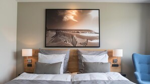 A hotel room with a large bed, two bedside tables with lamps, a blue armchair, and a framed picture of a beach scene on the wall. - Hotel 6400 (Sønderborg)