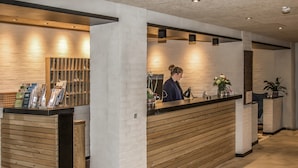 A reception desk with a wooden panel design, a white brick wall, and a reception area with a counter and a plant. - Hotel 6400 (Sønderborg)
