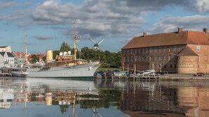 A historic ship docked at a harbor with a windmill and traditional buildings in the background. - Hotel 6400 (Sønderborg)