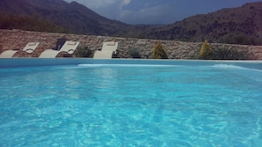 A swimming pool with clear blue water, surrounded by stone walls and lounge chairs. - Lake Villas (Apokoronas)