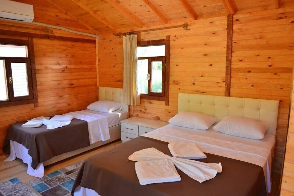 A wooden cabin with two single beds, a large bed, and a window with curtains.