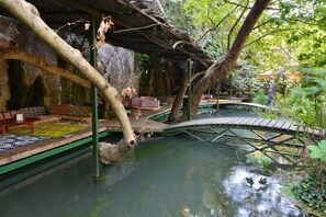 A naturalistic indoor setting with a water feature, wooden bridges, and seating areas. - Gorge Club Saklikent - Campsite (Kas)