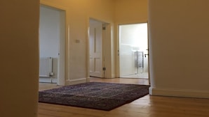 Un couloir doté d’un plancher en bois et d’un tapis à motifs, qui mène à une porte avec un radiateur et une fenêtre.