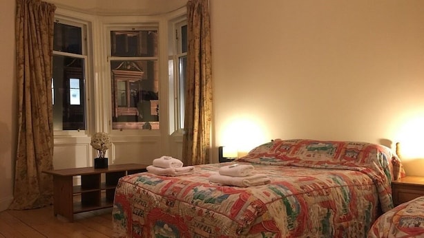 Une chambre à coucher avec un grand lit, deux tables de chevet, une commode et une fenêtre avec des rideaux.