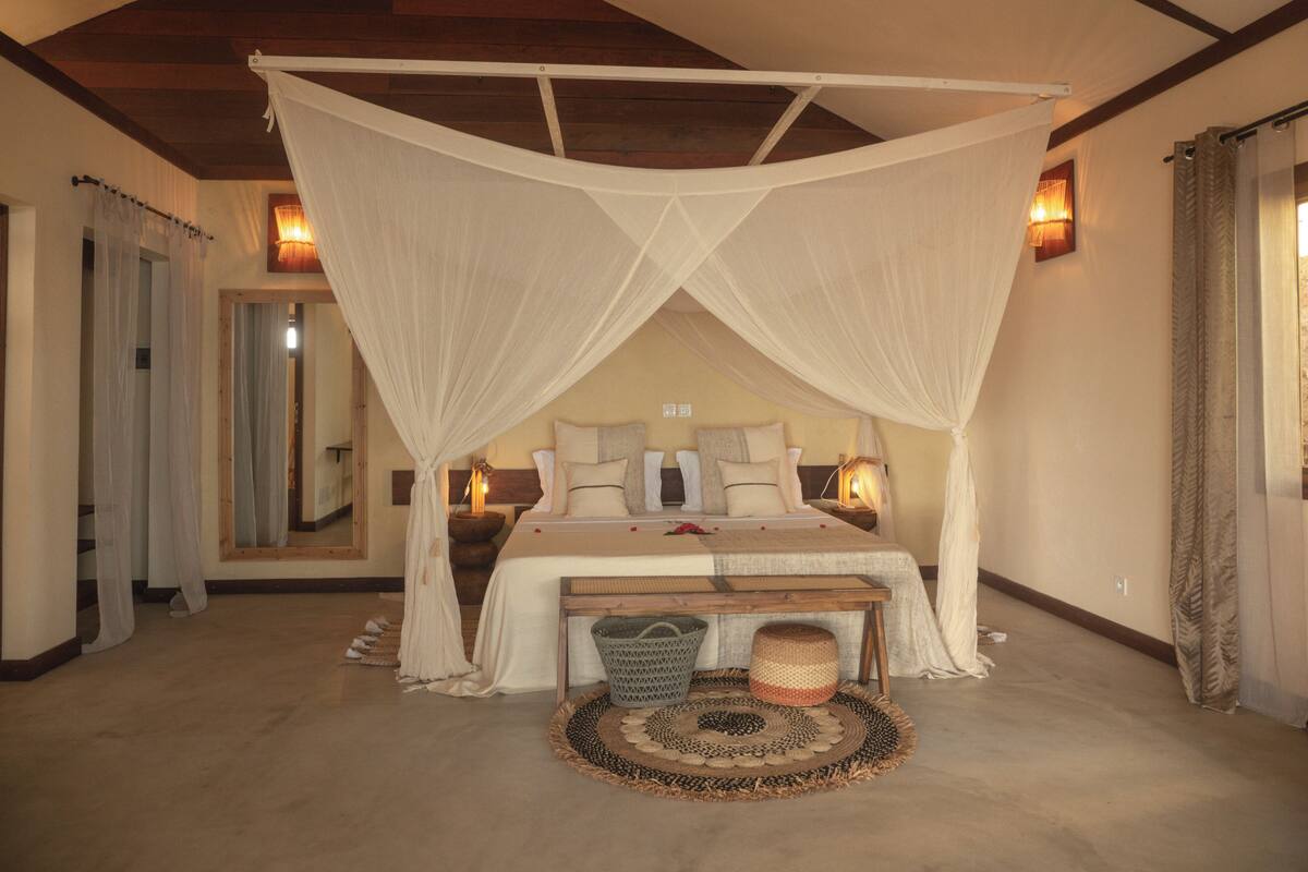 Un dormitorio amplio con cama a dosel, lámparas de noche y un espejo grande.