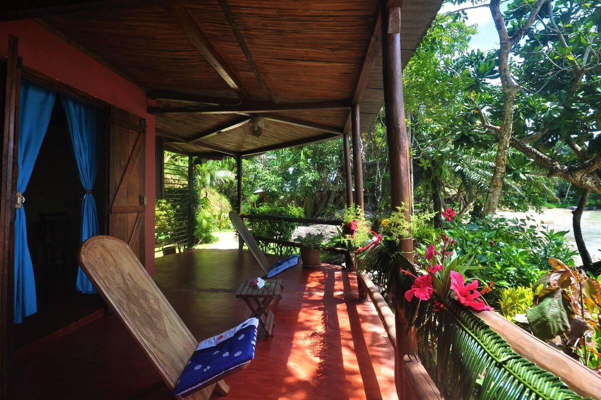 Un espacio al aire libre techado con muebles de madera y vista a follaje exuberante.