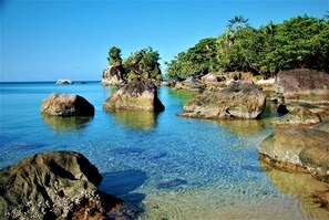 A clear view of a tropical beach with large rocks in the water and lush greenery on the shore. - Natiora Green Lodge (Nosy Boraha)