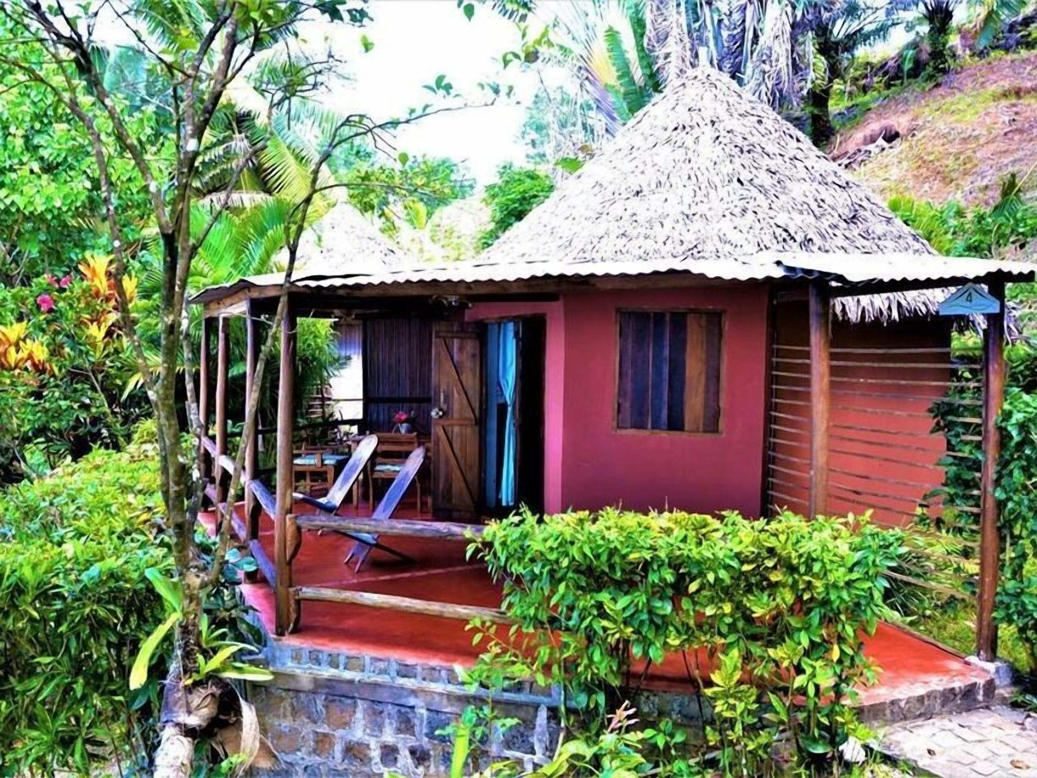 A small, rustic hut with a thatched roof, surrounded by lush greenery.