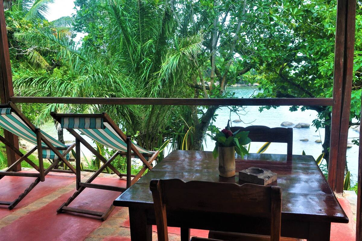 Una mesa de madera con una silla, un sillón a rayas y vistas a un río y follaje.