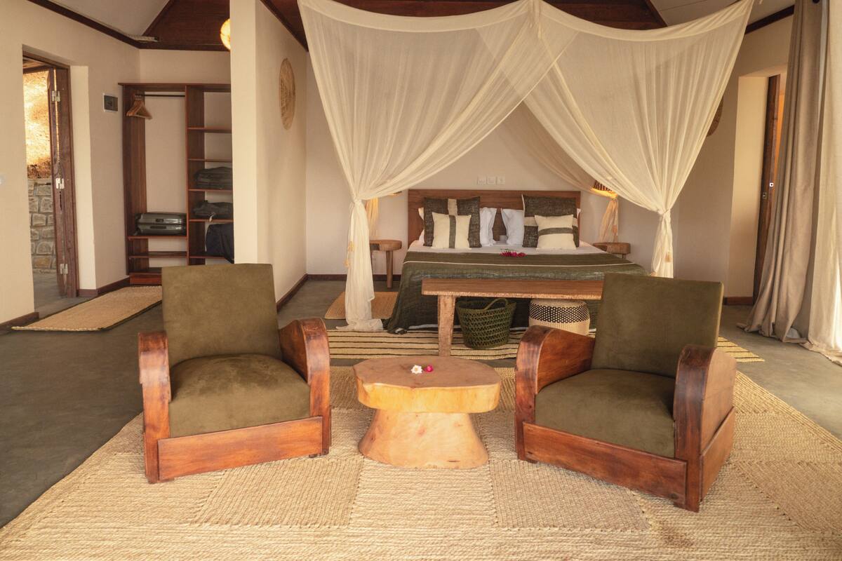 Una habitación con una cama, dos sillones, una pequeña mesa de madera y un dosel sobre la cama.