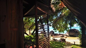 Una estructura de madera con techo de listones que da a una playa con rocas y vegetación.