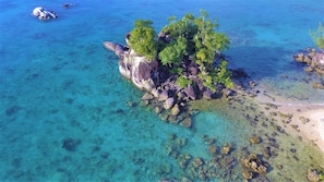 A clear aerial view of a small island with rocky terrain and dense vegetation, surrounded by turquoise waters. - Natiora Green Lodge (Nosy Boraha)