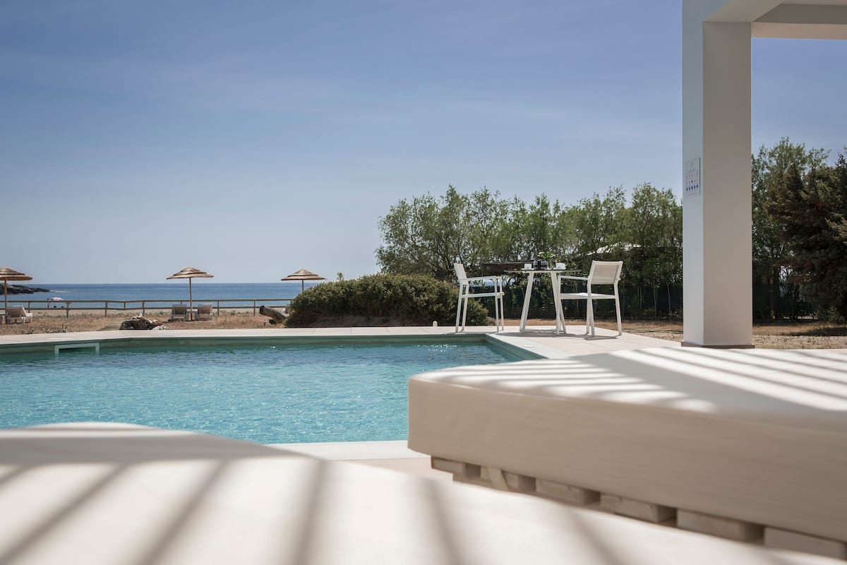 Zona junto a la piscina con vista al mar, sillas de descanso y sombrillas.
