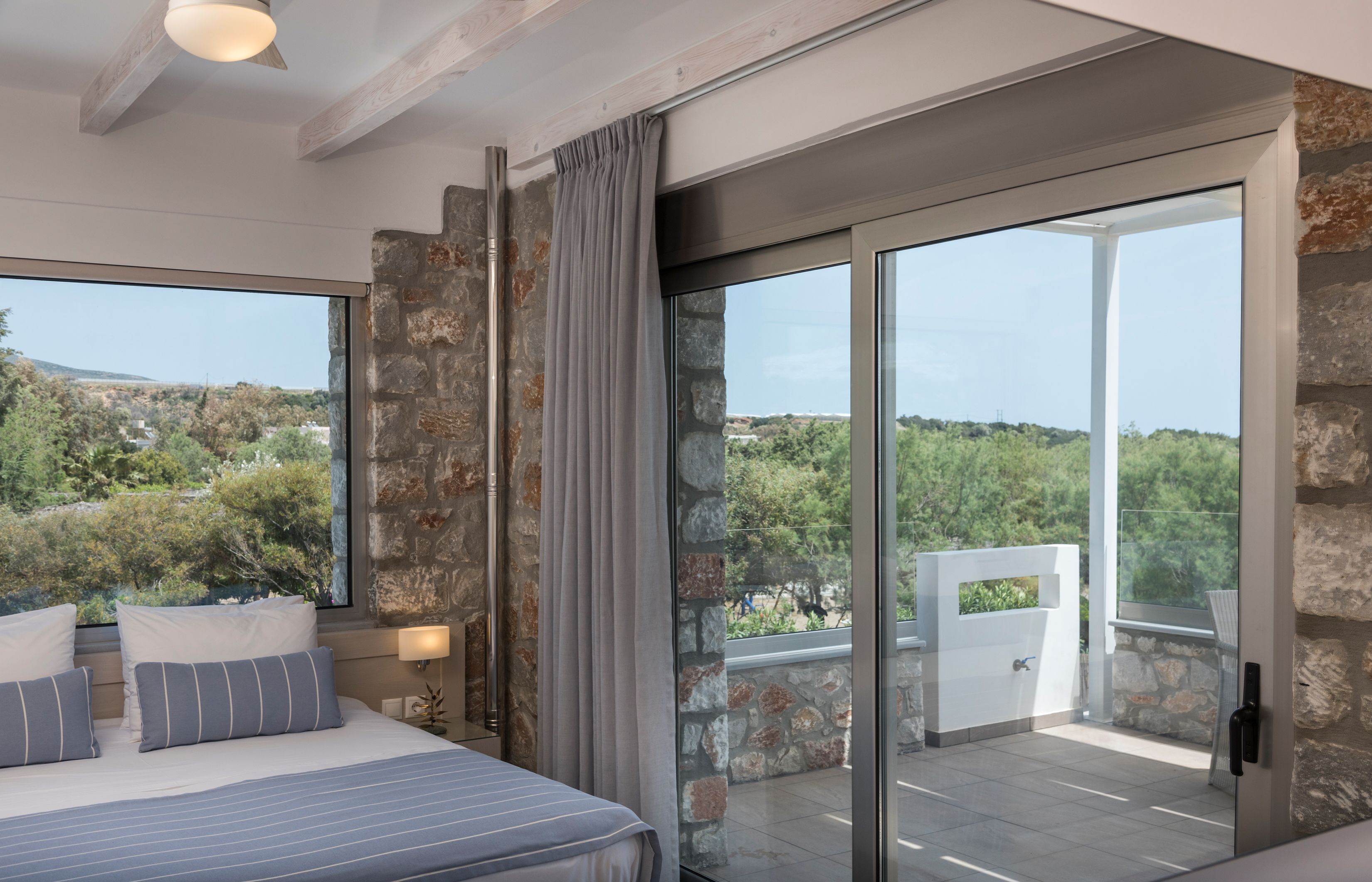 A modern bedroom with a large bed, a view of greenery outside, and a sliding glass door leading to an outdoor area.