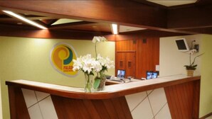 A reception desk with a logo, a vase of flowers, and a wooden panel design. - Serra Negra Paladium Hotel (Serra Negra)