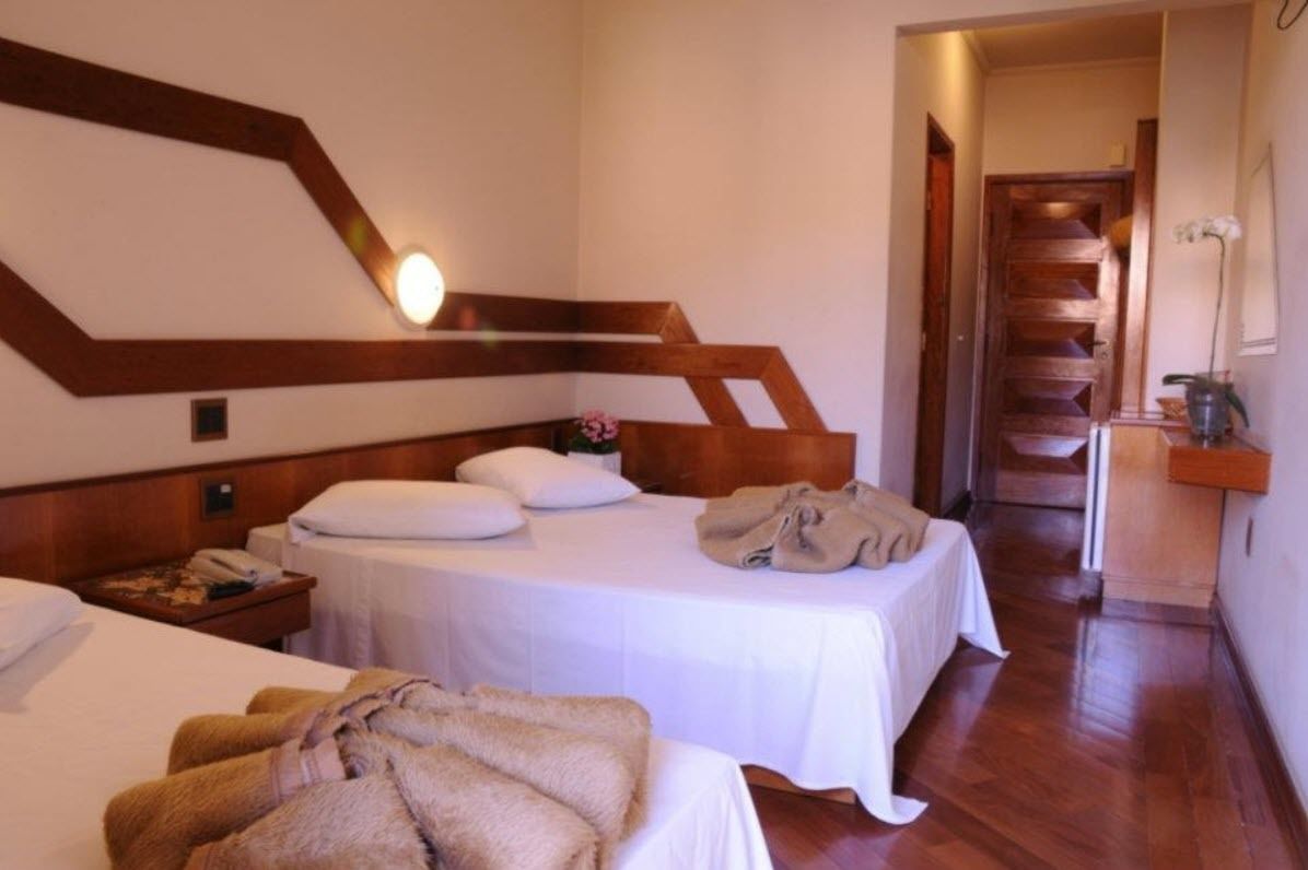 Quarto de hotel com duas camas, cabeceiras de madeira, uma escada e uma pequena mesa com um vaso.