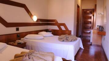 Quarto de hotel com duas camas, cabeceiras de madeira, uma escada e uma pequena mesa com um vaso.