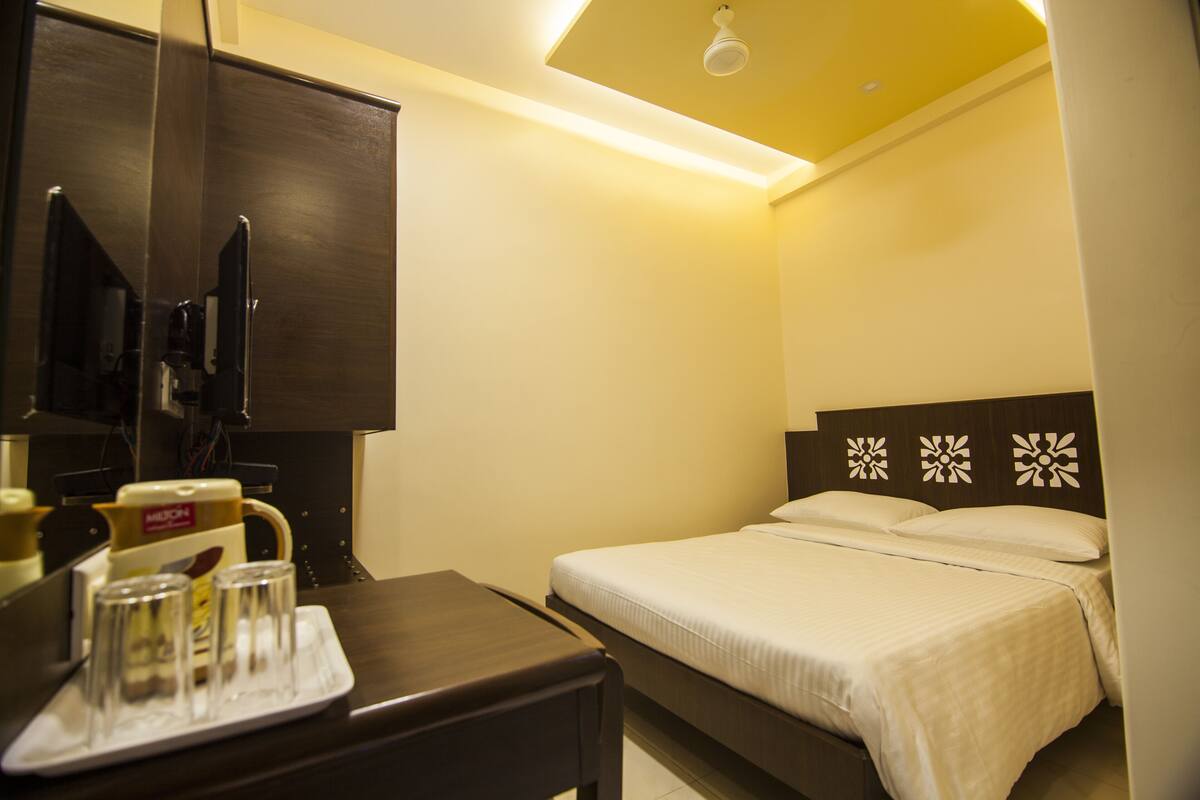 A hotel room with a bed, a desk with a coffee maker, and a television.