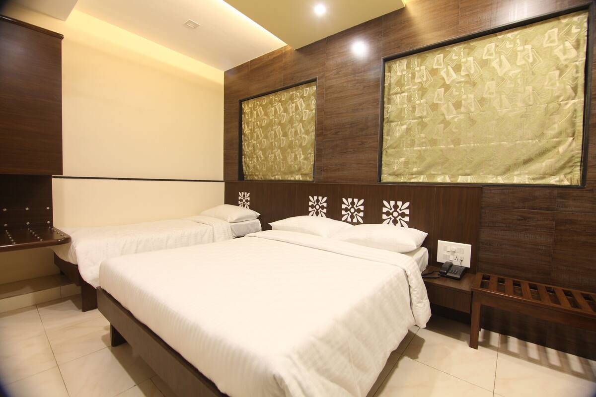 A hotel room with two beds, a wooden headboard, a bedside table with a phone, and a wall-mounted light fixture.