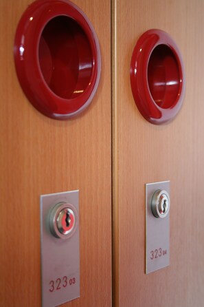 Zwei Türen mit roten Griffen und einem Zifferncode-Schloss, jede mit der Nummer 323 beschriftet.