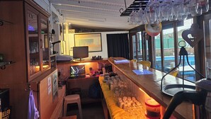 A bar area with a wooden counter, a computer, and various glasses and bottles. - Nil Hotel (Ayvalik)