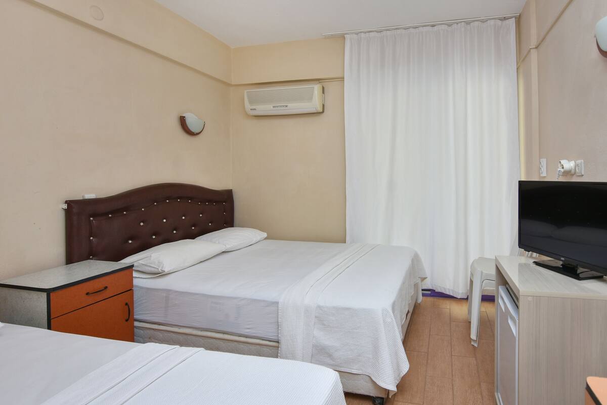 A hotel room with two beds, a TV, and an air conditioning unit.