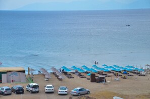 A beach with umbrellas, cars, and a building labeled "OMEGA HOTEL". - Nil Hotel (Ayvalik)