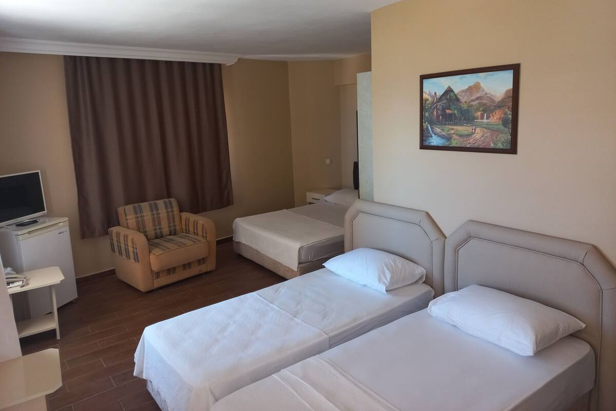 A hotel room with two single beds, a small desk with a computer, a chair, and a painting on the wall.