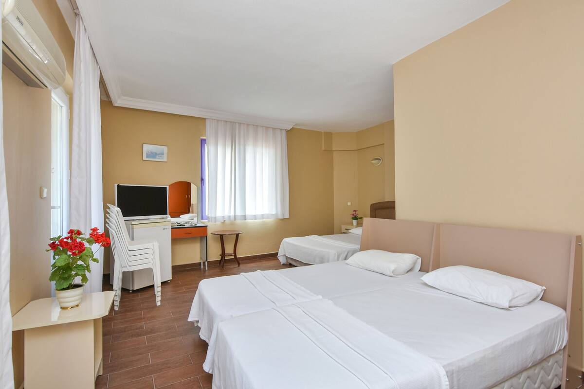 A hotel room with two beds, a desk with a computer, a chair, and a window with curtains.