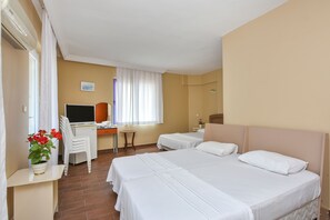 A hotel room with two beds, a desk with a computer, a chair, and a window with curtains. - Nil Hotel (Ayvalik)