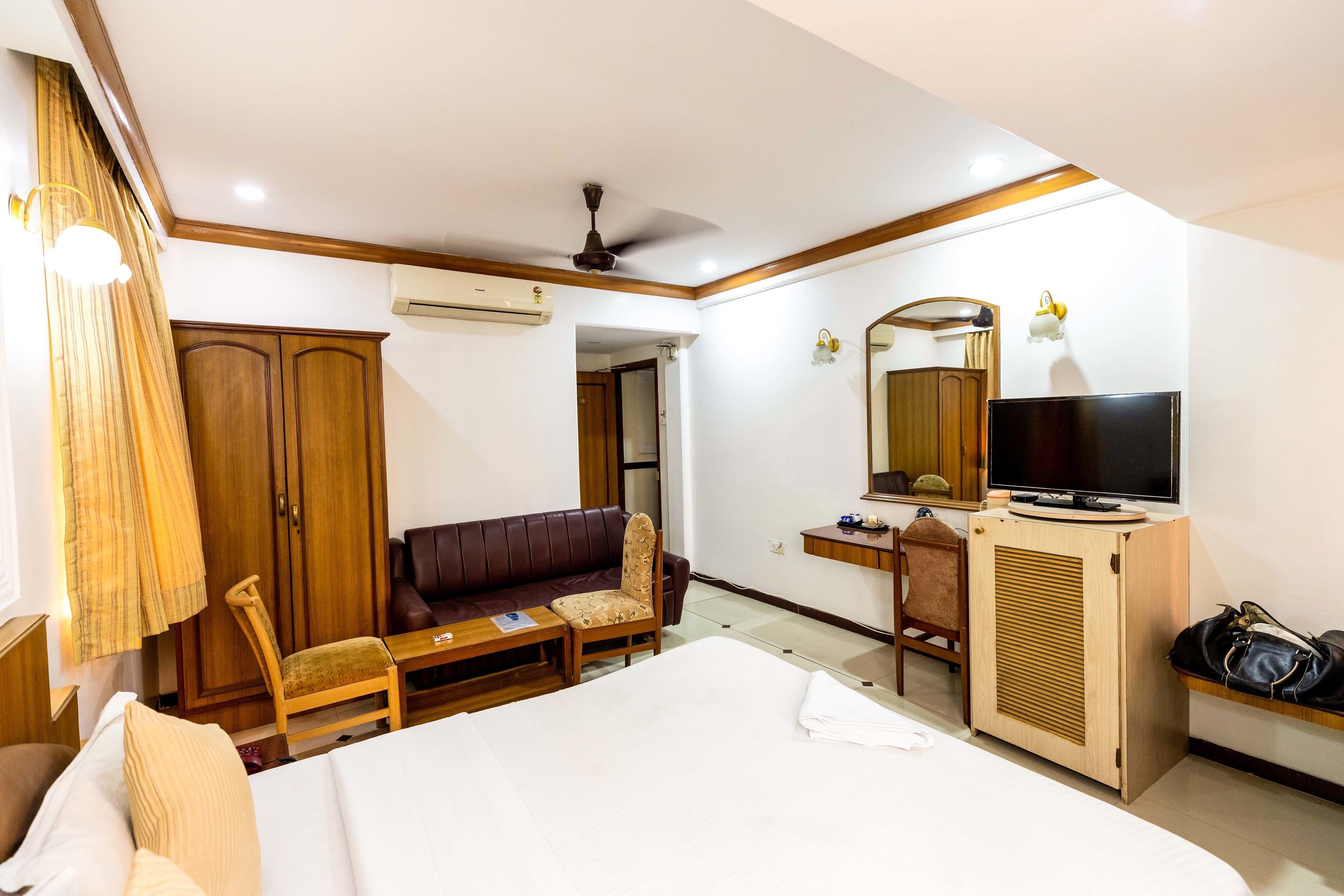 A hotel room with a bed, a desk, a television, a wardrobe, and a seating area.