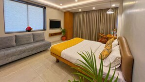 Una habitación de hotel moderna con una cama grande, un sofá, un televisor montado en la pared y una ventana con cortinas.