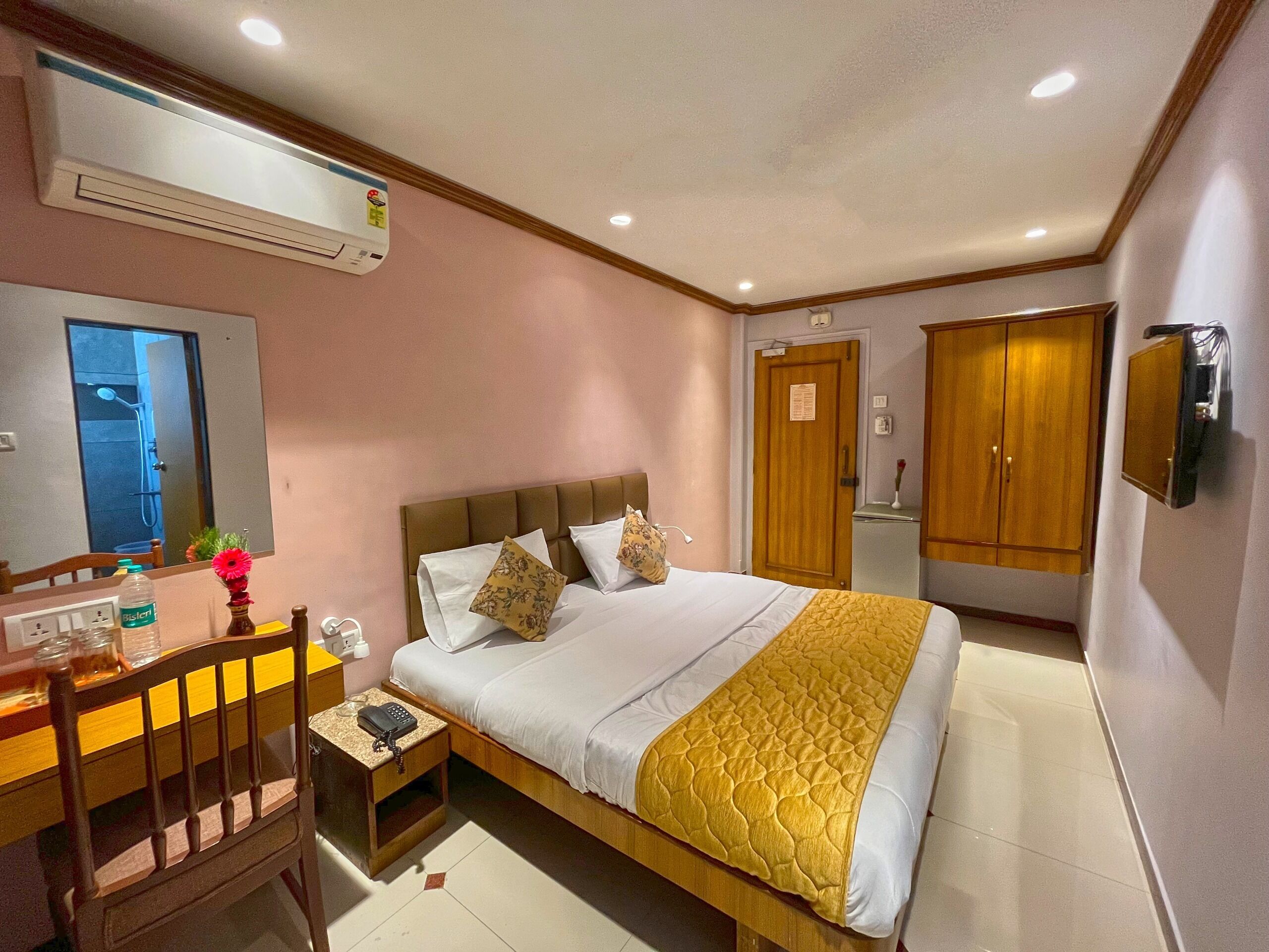 A hotel room with a bed, bedside table, chair, desk, and a mirror.