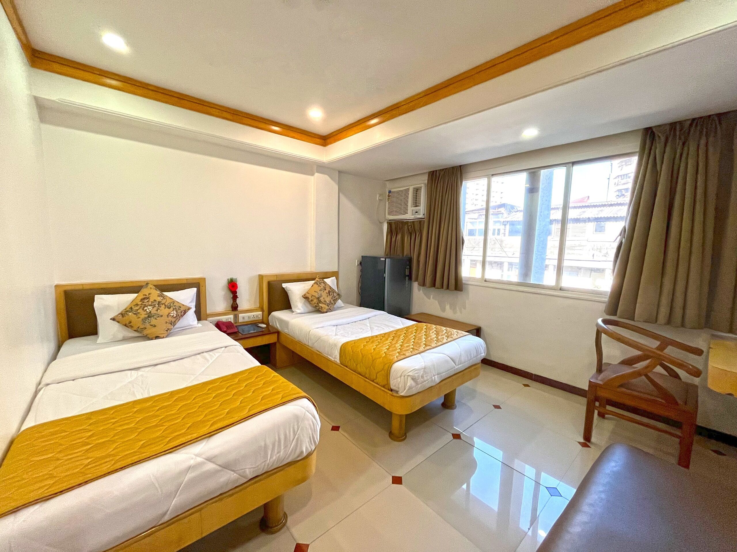 Habitación de hotel con dos camas, un escritorio, una silla, ventana con cortinas y aire acondicionado.