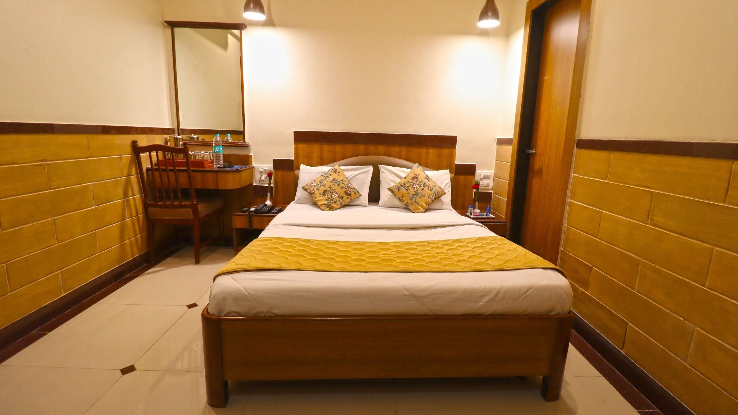 Een hotelkamer met een houten bed, een bureau met stoel, een spiegel en een nachtkastje met lamp en telefoon.