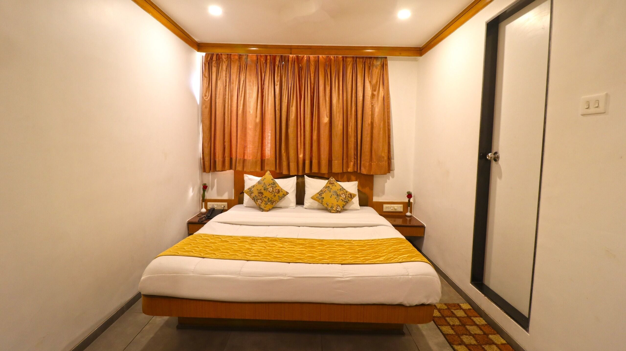 A hotel room with a bed, curtains, a nightstand, and a door.