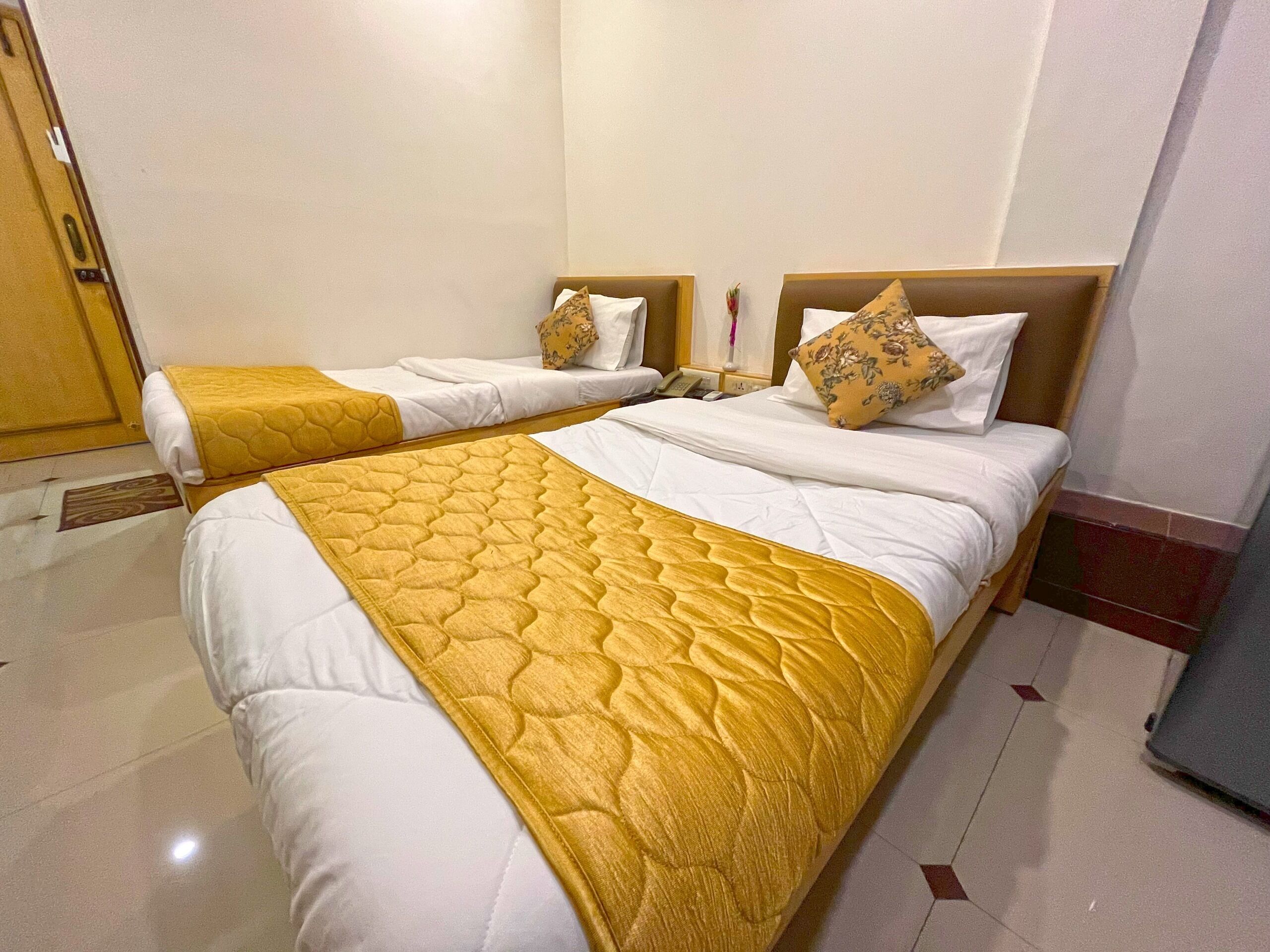 A hotel room with two beds, each with white bedding and a yellow quilt.