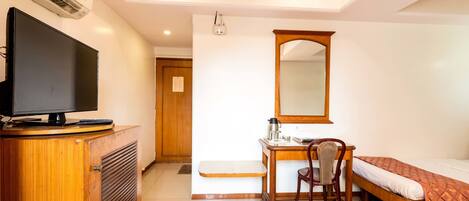A hotel room with a wooden desk, a chair, a bed, a television on a cabinet, and a ceiling fan.