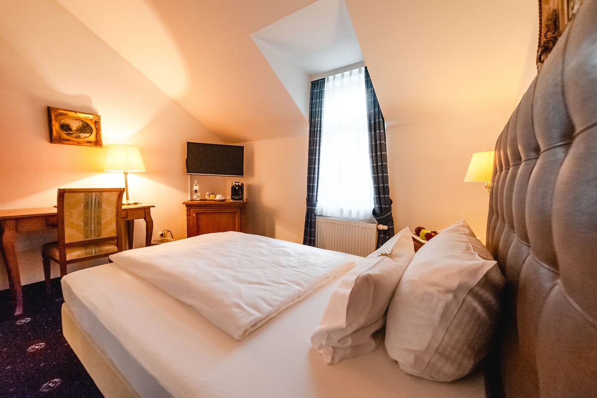 A hotel room with a bed, a desk, a chair, a television, and a window with curtains.