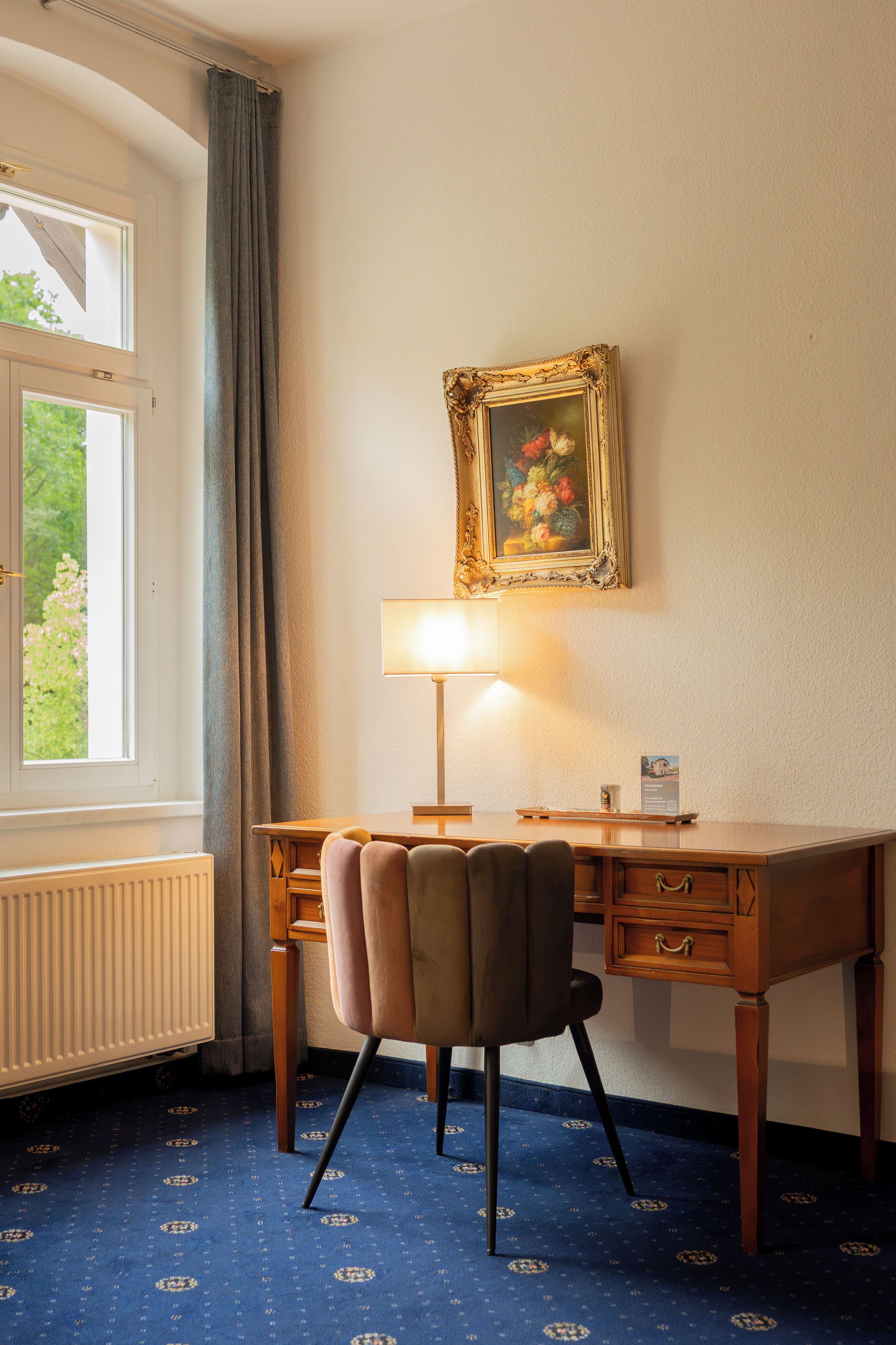 Una habitación de hotel con escritorio, silla, lámpara y un cuadro en la pared.