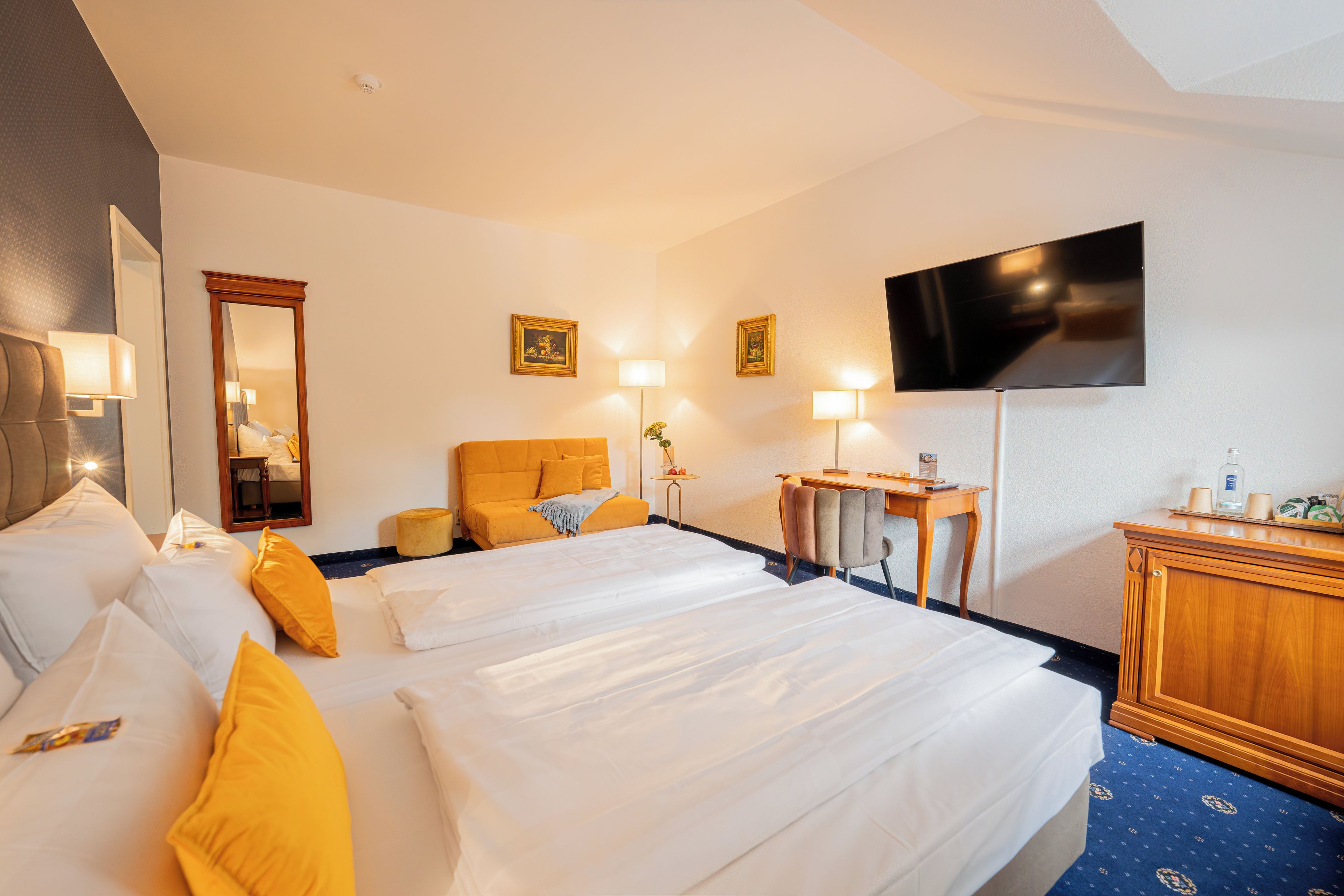 A hotel room with two beds, a desk, a television, and a mirror.