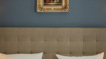 A hotel room with a headboard, two white pillows, and a framed floral artwork on the wall.
